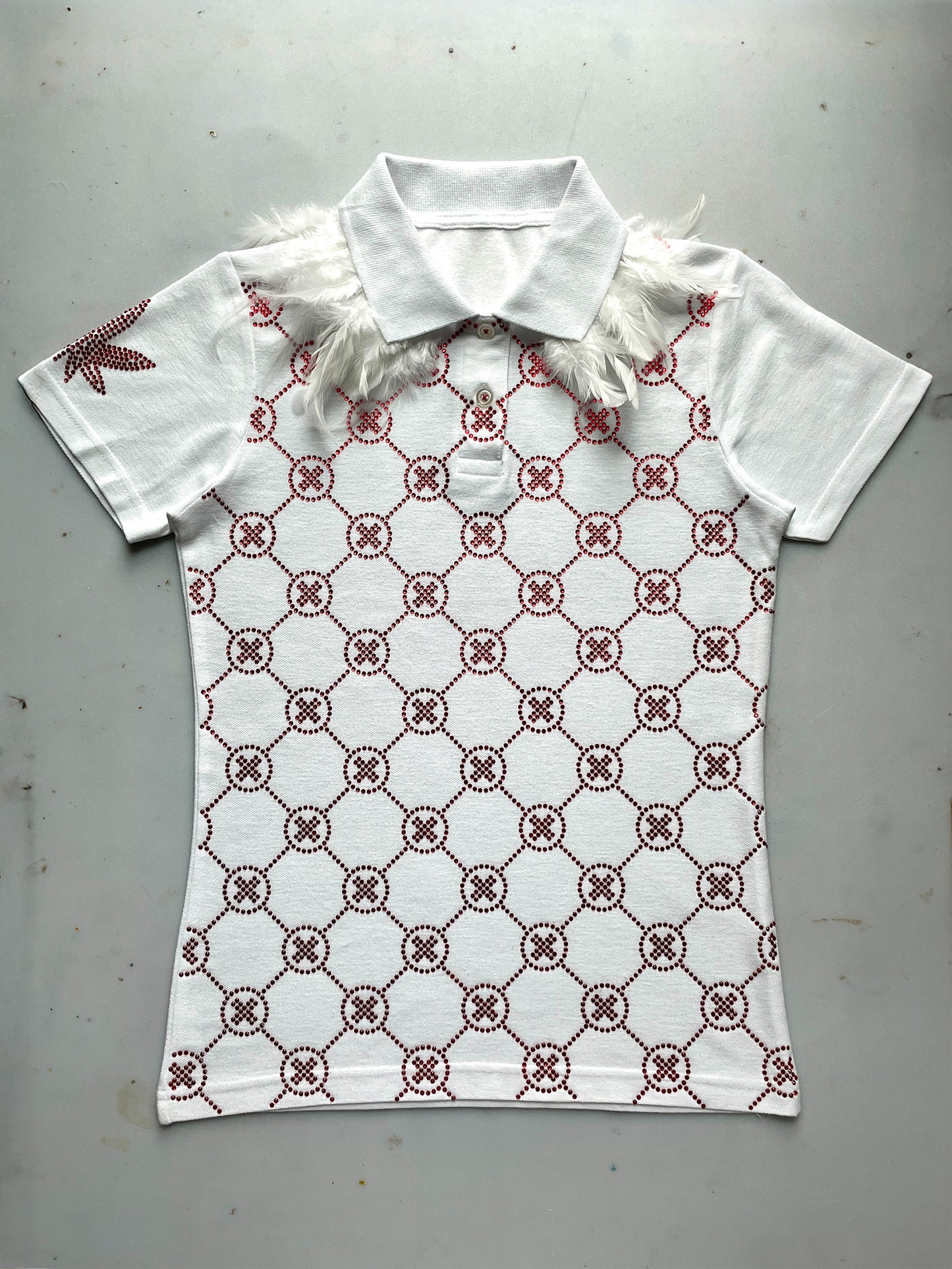 Witte polo met rode crystal gems, all-over monogram patroon en veren details op de schouders.